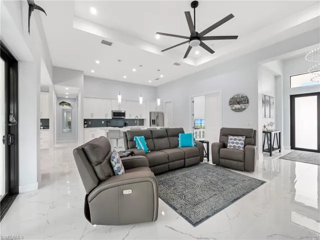 Living area with ceiling fan, light marble finish floors, a chandelier, and a raised ceiling