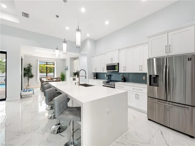 Kitchen featuring stainless steel appliances, a kitchen breakfast bar, a large island with sink, white cabinetry, and decorative light fixtures