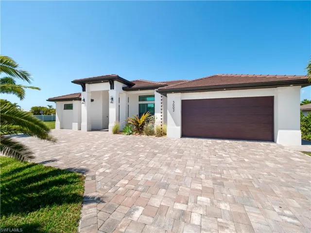 Prairie-style house with an attached garage, decorative driveway, stucco siding, and a tiled roof