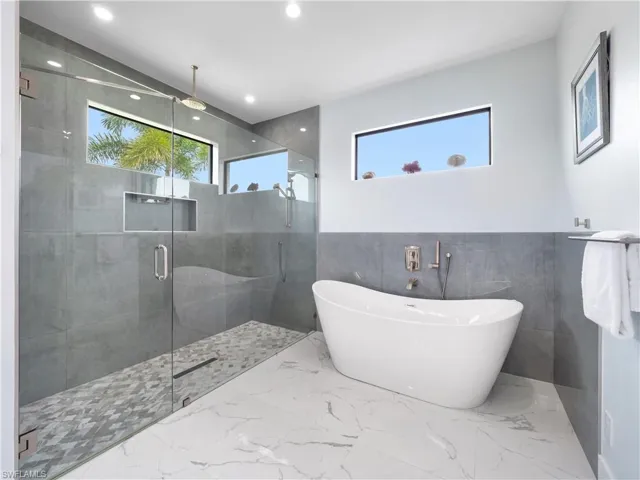 Bathroom featuring tile walls, healthy amount of natural light, marble finish flooring, a shower stall, and a freestanding tub