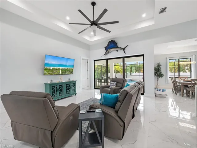 Living area featuring a ceiling fan, recessed lighting, a tray ceiling, and light marble finish flooring