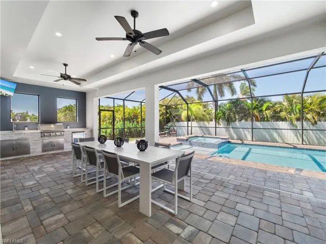 Fenced backyard with an outdoor kitchen / dining area, a patio, a pool with connected hot tub, a sunroom, and glass enclosure
