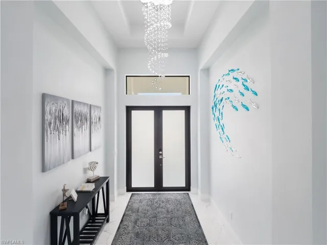 Doorway with hanging lights, marble finish flooring, a raised ceiling, and french doors