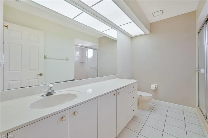 Bathroom with a skylight, toilet, tile patterned flooring, vanity, and a shower stall