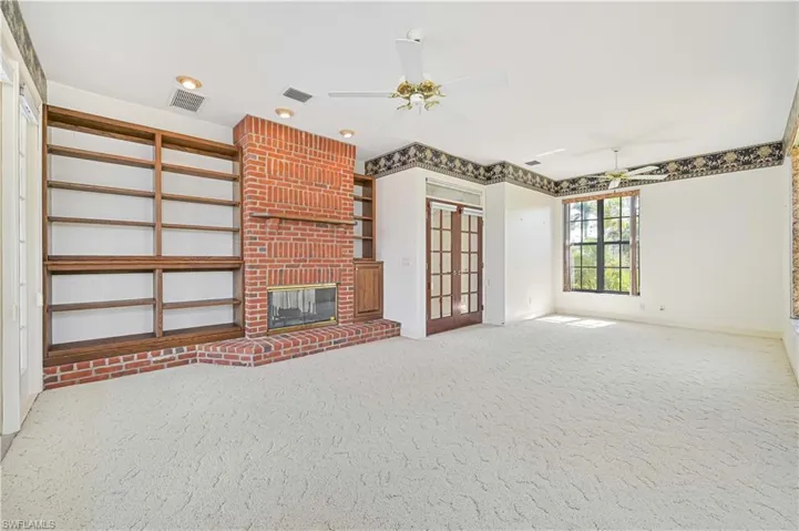 Unfurnished living room with a brick fireplace, carpet, visible vents, and a ceiling fan