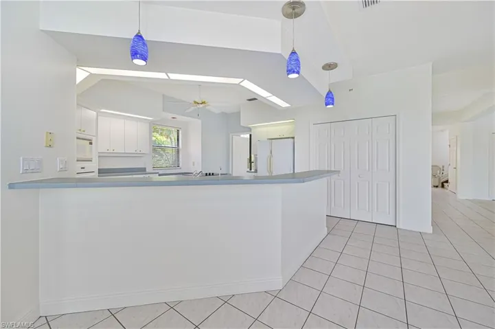 Kitchen featuring white appliances, ceiling fan, a peninsula, white cabinetry, and pendant lighting