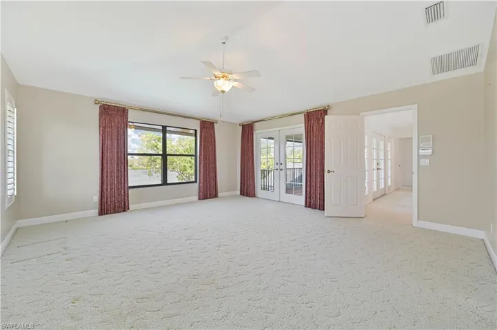 Empty room featuring french doors, visible vents, vaulted ceiling, and light carpet