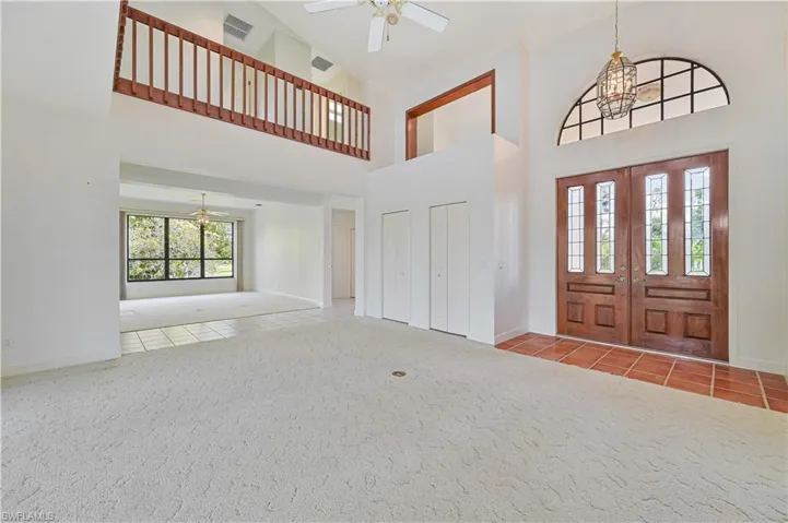 Carpeted foyer entrance with visible vents, baseboards, a towering ceiling, tile patterned floors, and ceiling fan with notable chandelier