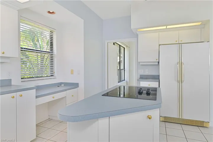 Kitchen with black electric stovetop, light tile patterned flooring, a kitchen island, built in study area, and freestanding refrigerator