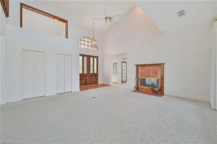 Carpeted entryway with visible vents, a tiled fireplace, a ceiling fan, high vaulted ceiling, and baseboards