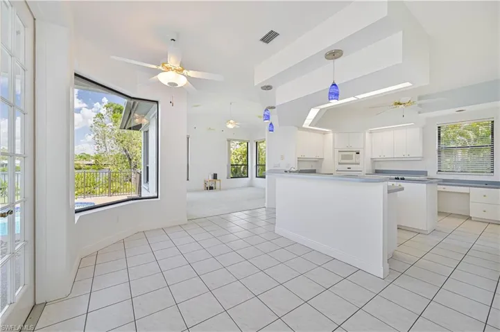 Kitchen featuring light tile patterned floors, visible vents, white microwave, white cabinets, and ceiling fan