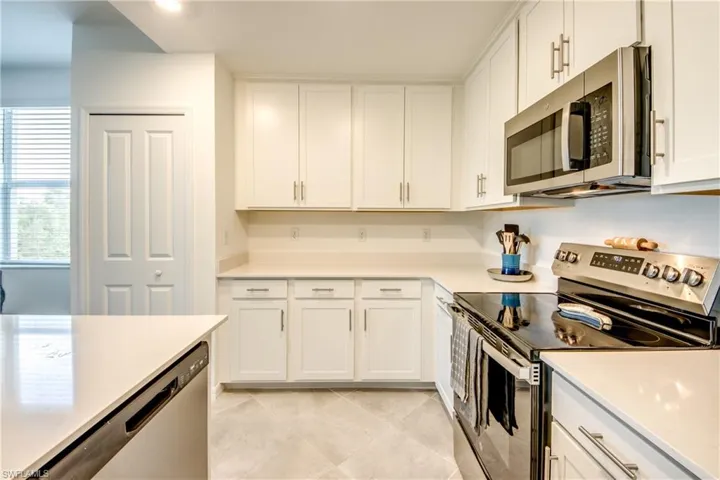 Kitchen with stainless steel appliances, white cabinets, light stone counters, and light tile patterned flooring