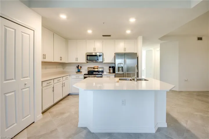 Kitchen featuring stainless steel appliances, a center island with sink, white cabinetry, recessed lighting, and light stone countertops