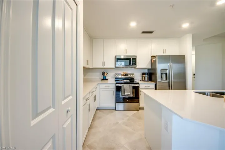 Kitchen with stainless steel appliances, white cabinetry, and light stone countertops