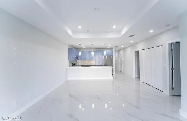 Kitchen featuring a peninsula, hanging light fixtures, a raised ceiling, freestanding refrigerator, and light marble finish flooring