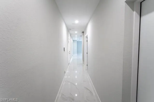 Hallway with a textured wall, marble finish flooring, and recessed lighting