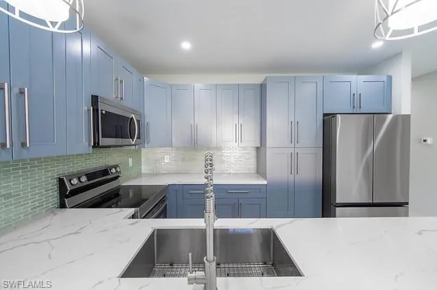 Kitchen featuring stainless steel appliances, light stone counters, hanging light fixtures, and blue cabinets