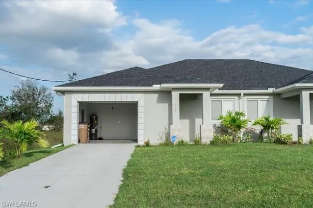 View of front facade with stucco siding, a front lawn, concrete driveway, an attached garage, and water heater