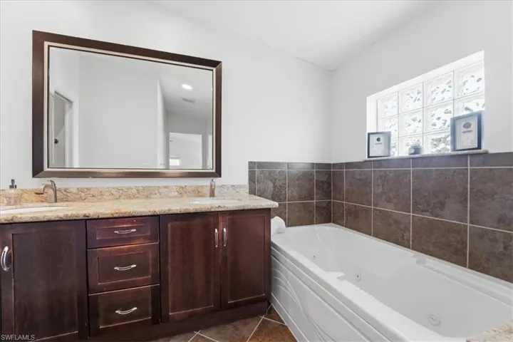 Bathroom featuring a tub with jets, double vanity, and dark tile patterned flooring
