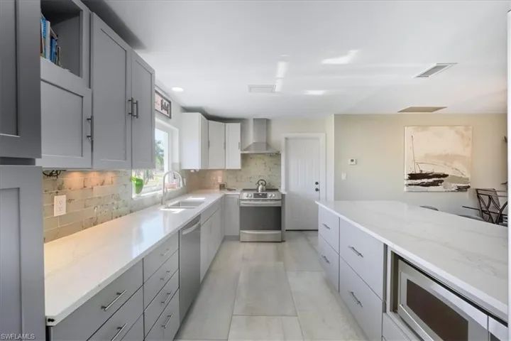 Kitchen with gray cabinetry, stainless steel appliances, light stone counters, and wall chimney range hood