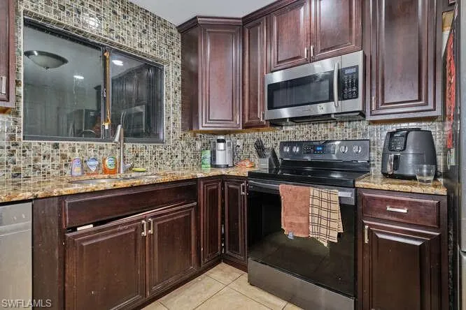 Kitchen with backsplash, dishwasher, range with electric cooktop, sink, and light tile floors