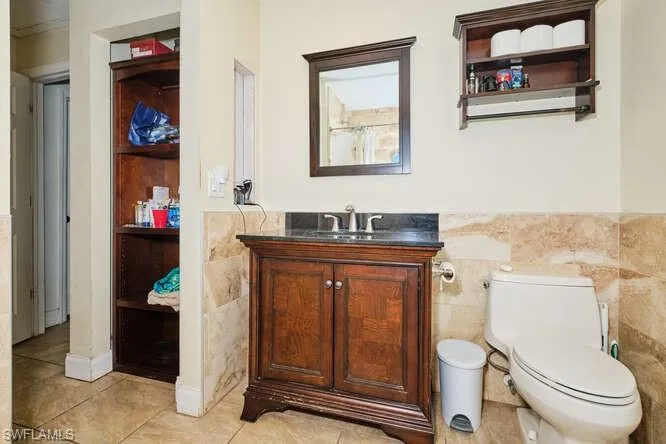 Bathroom with tile flooring, vanity, toilet, and tile walls