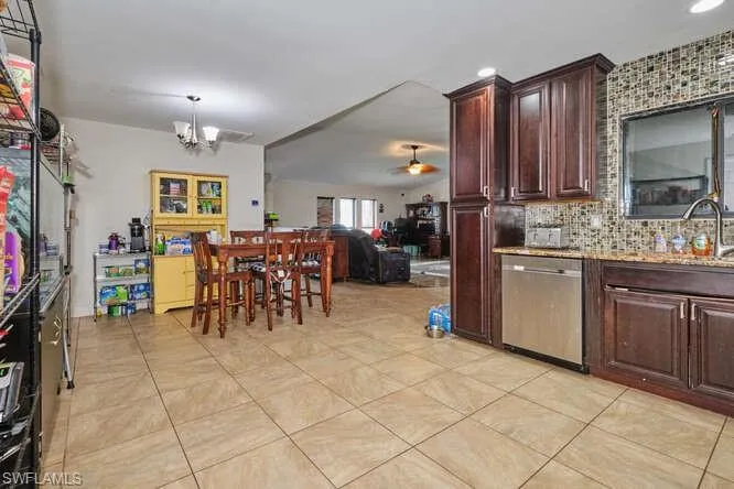 Kitchen with ceiling fan with notable chandelier, backsplash, sink, light tile flooring, and dishwasher