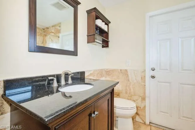 Bathroom featuring tile walls, tile floors, vanity, and toilet