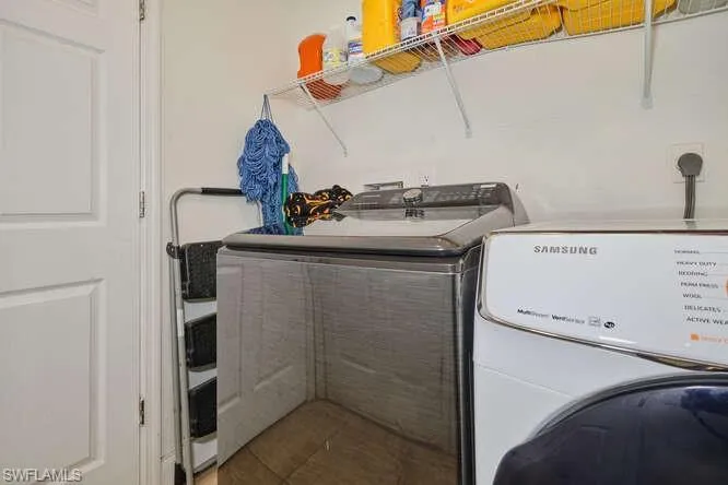 Clothes washing area featuring tile floors, washer and clothes dryer, and hookup for an electric dryer