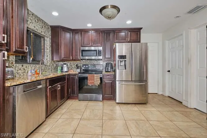 Kitchen with light stone countertops, stainless steel appliances, light tile flooring, backsplash, and sink