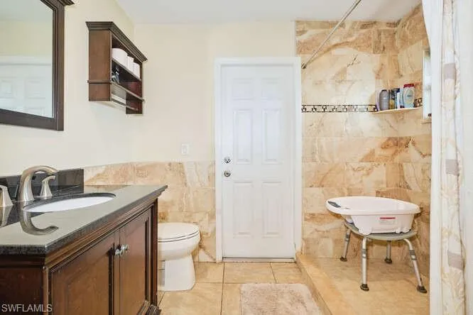 Bathroom featuring tile floors, vanity, toilet, and tile walls