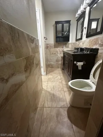 Bathroom with toilet, vanity, tile walls, tile patterned floors, and decorative backsplash