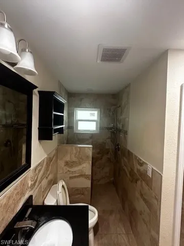 Bathroom with toilet, tile walls, tile patterned floors, sink, and a tile shower