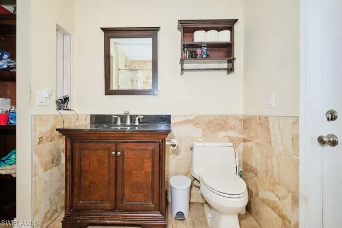 Bathroom featuring vanity, toilet, and tile walls