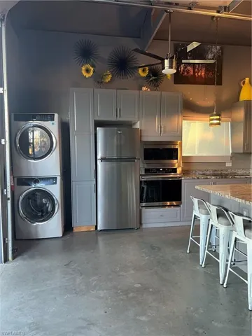 Kitchen featuring gray cabinets, stacked washing maching and dryer, stainless steel appliances, decorative light fixtures, and concrete flooring