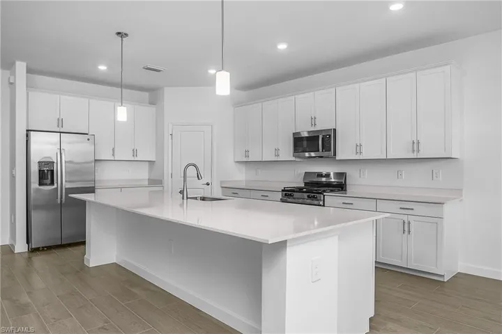 Kitchen with white cabinetry, stainless steel appliances, quartz countertops and walk-in pantry.