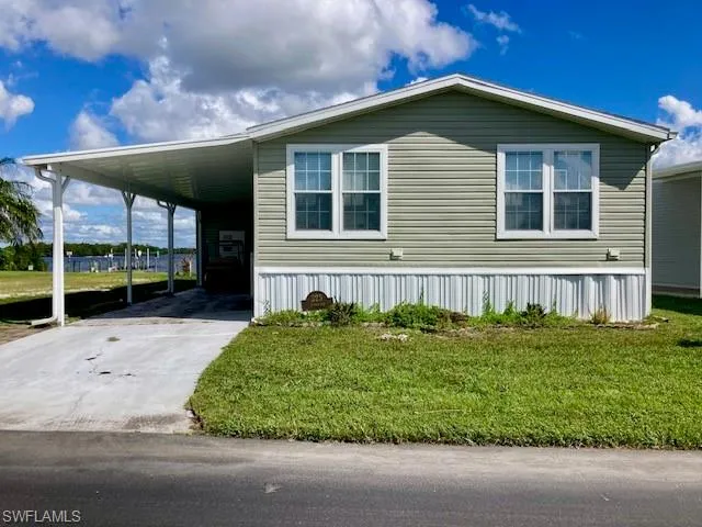 Manufactured / mobile home featuring a front lawn, driveway, and a carport