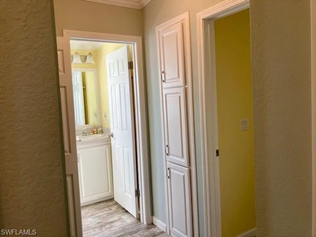 Hallway with a textured wall, light wood-style flooring, and crown molding