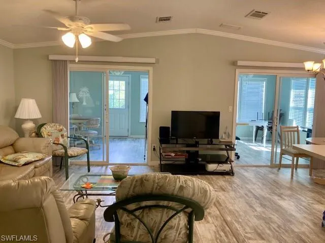 Living room with crown molding, lofted ceiling, wood finished floors, and ceiling fan