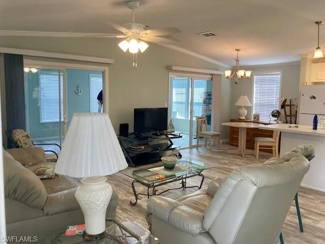 Living room with ornamental molding, vaulted ceiling, a ceiling fan, light wood finished floors, and a chandelier