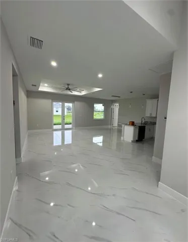 Spare room with a tray ceiling, ceiling fan, recessed lighting, and light marble finish flooring
