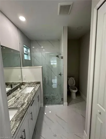 Full bathroom with double vanity, a marble finish shower, light marble finish floors, and recessed lighting