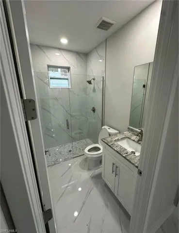 Bathroom with light marble finish flooring, vanity, a marble finish shower, and recessed lighting