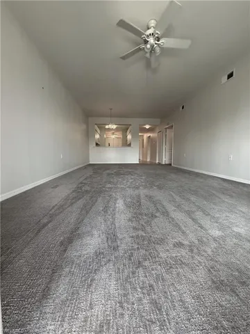 Unfurnished living room with dark colored carpet, a chandelier, and ceiling fan