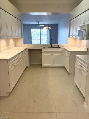 Kitchen featuring white cabinetry, light countertops, white microwave, and light tile patterned floors