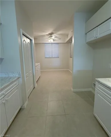 Kitchen with white cabinetry, light tile patterned floors, light stone counters, and ceiling fan
