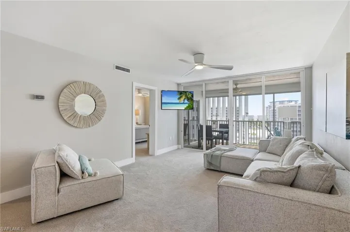 Carpeted living space with a ceiling fan, wall-mounted television, and direct access to a balcony with sliding glass doors - Virtually Edited Image