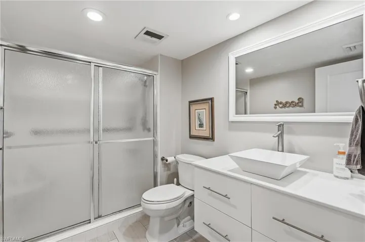 Shower with sliding frosted glass doors, white rectangular vessel sink, white vanity with contemporary hardware, wall-mounted mirror with white frame, and recessed lighting - Virtually Edited Image