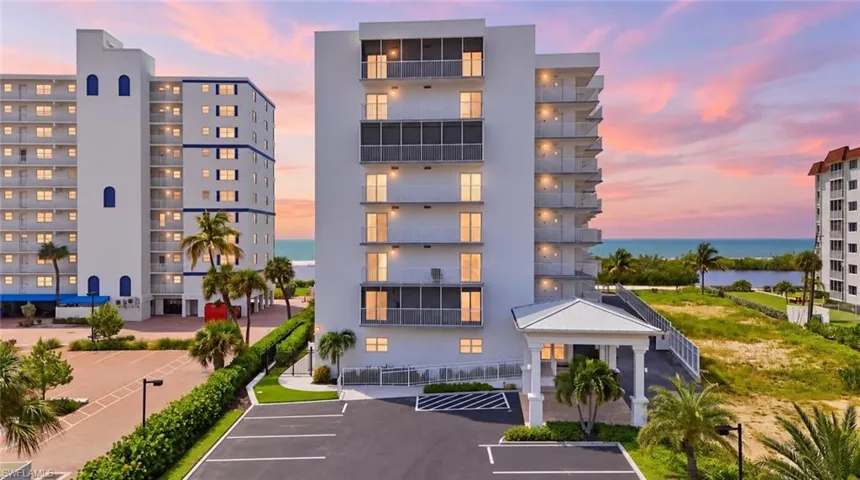 Multi-story building with multiple private balconies, a covered entryway, and an asphalt parking area - Virtually Edited Image