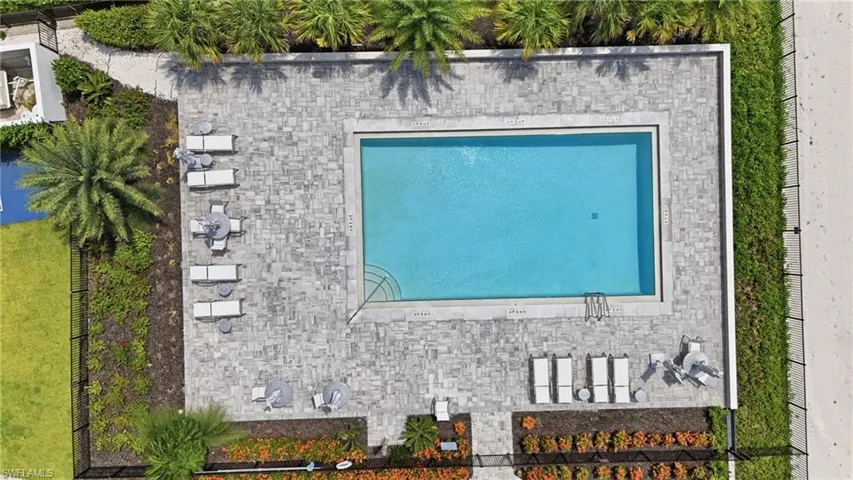 Rectangular swimming pool surrounded by paver decking, enclosed by a black metal fence, with surrounding landscaping and palm trees - Virtually Edited Image